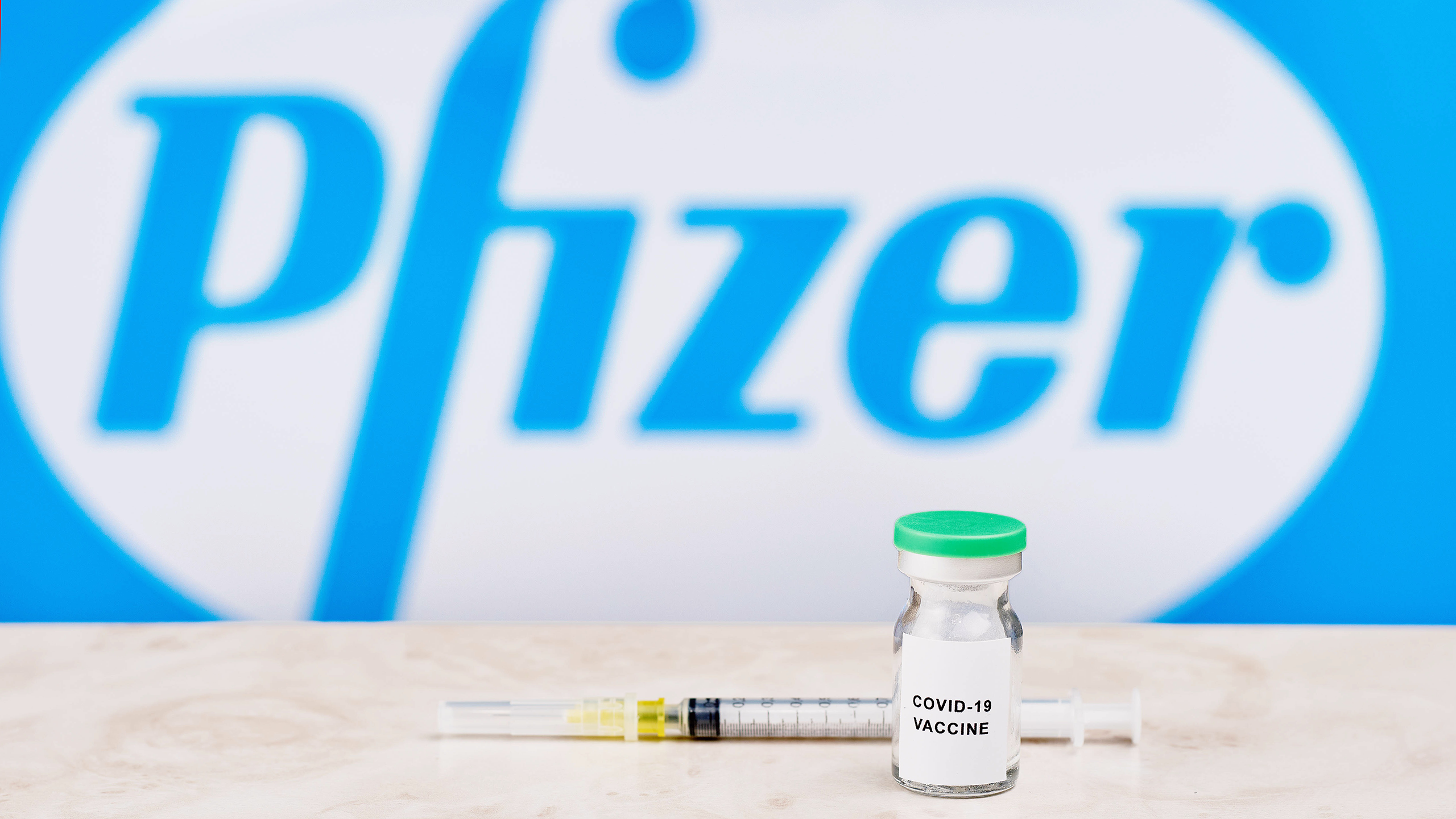 Photo of a COVID-19 vaccine in front of a Pfizer logo