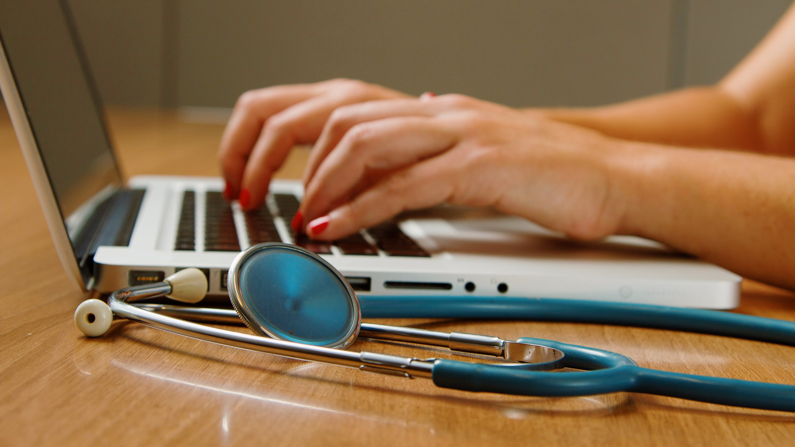 Photo of a person typing on a laptop next to a stethoscope