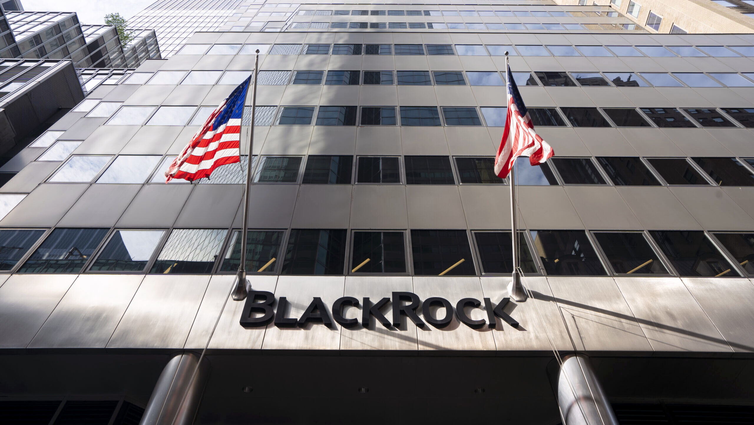 The front of BlackRock's headquarters in downtown New York City is shown, with two American flags hanging over the front entrance.
