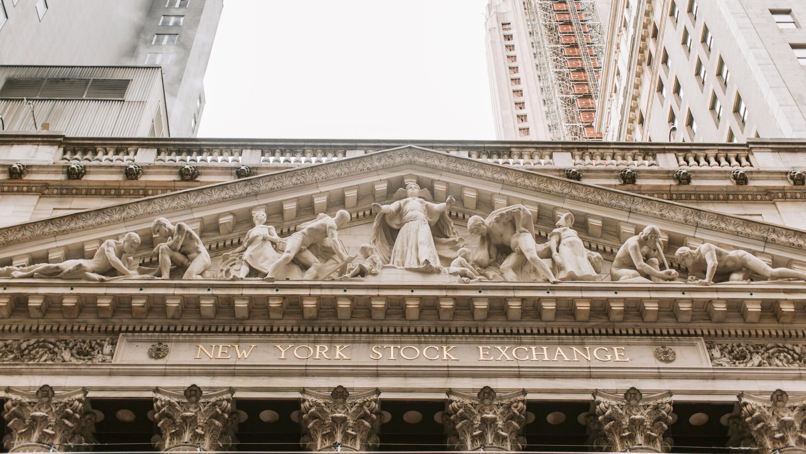 The facade of the New York Stock Exchange in New York City is shown, with multiple marble figures representing parts of the economy including industry, agriculture and mining situated above the entrance.