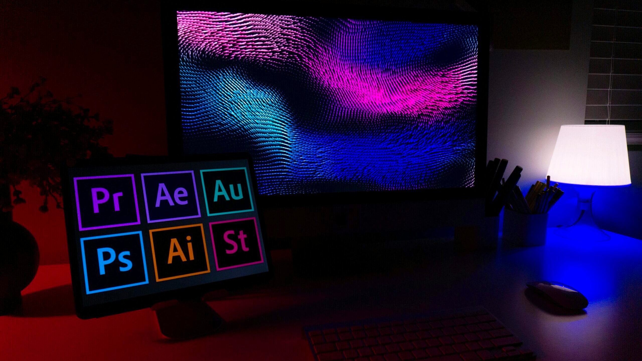 A tablet screen in front of a large computer display shows the icons for several Adobe software programs, including Photoshop.
