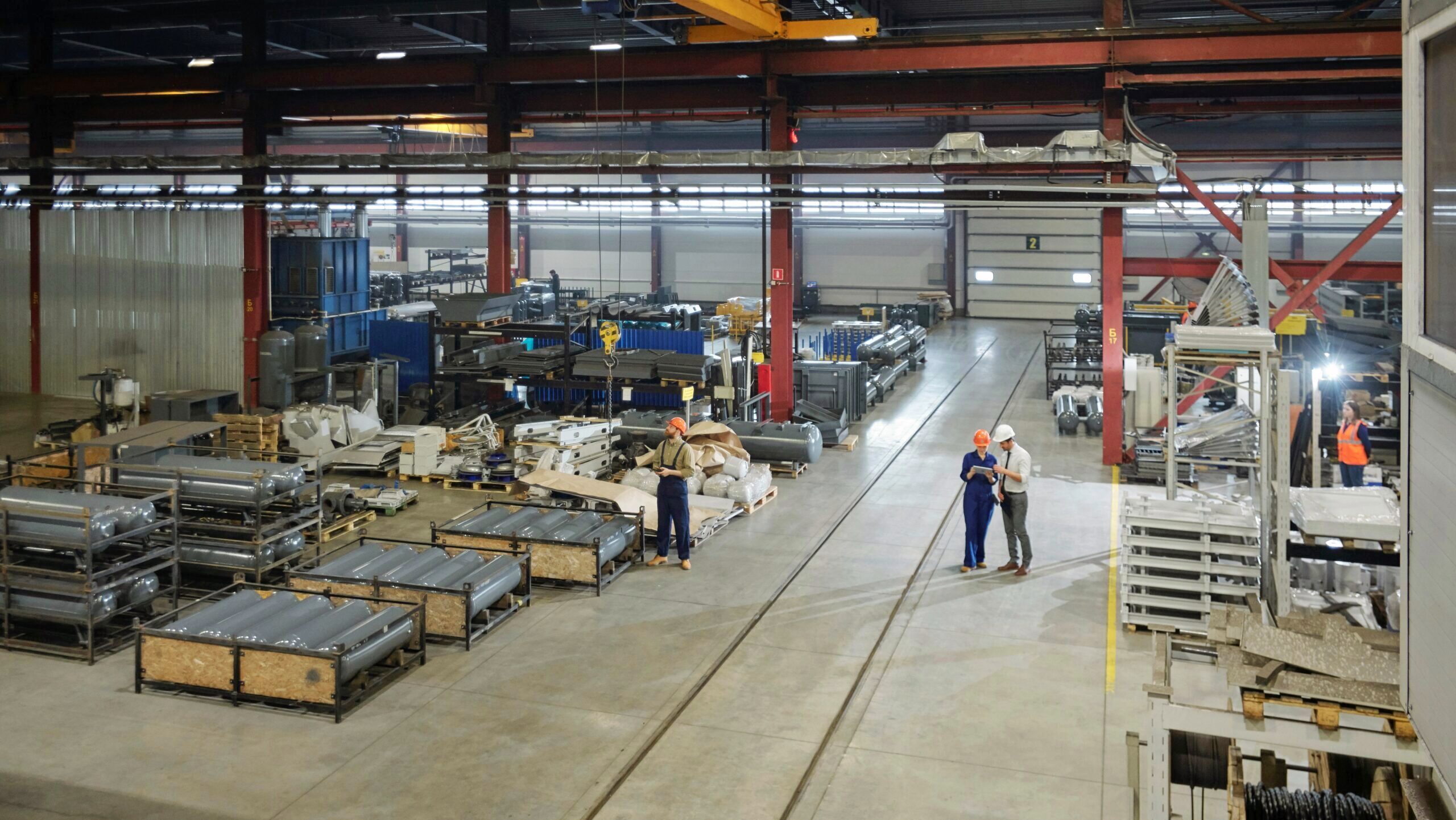 Several people with hardhats are seen standing in the warehouse of an air tank production factory.