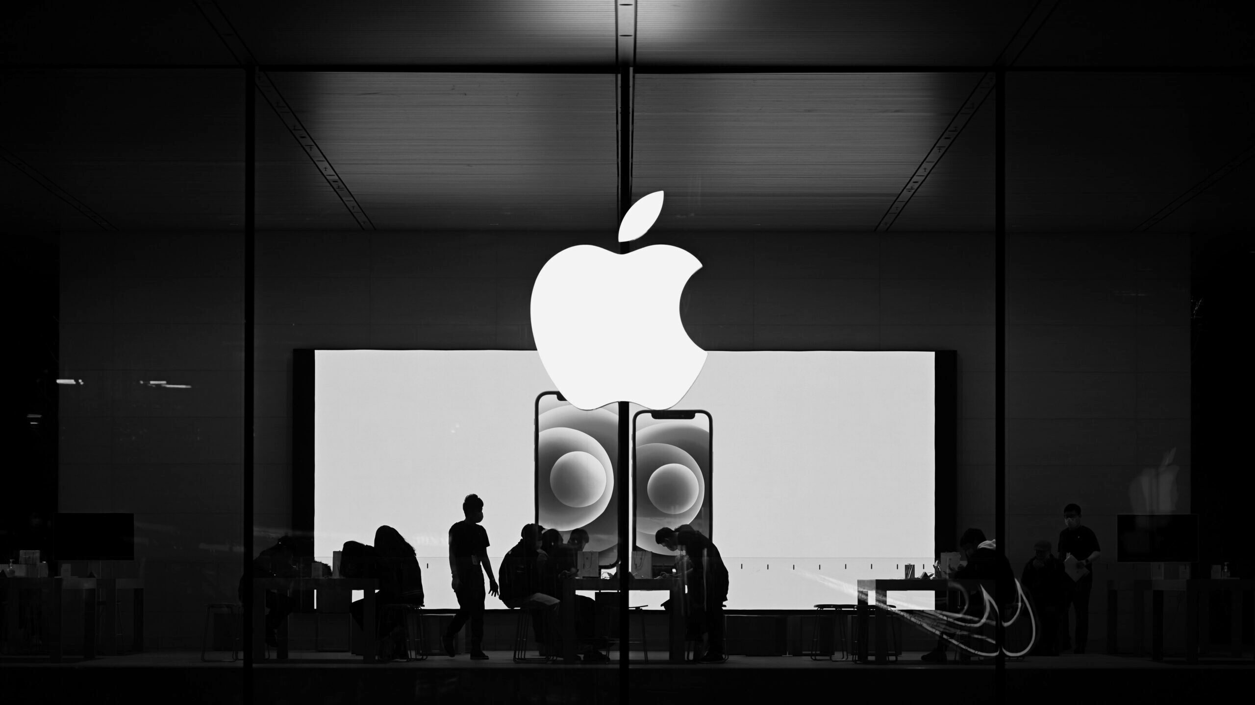 The silhouettes of several workers can be seen against the backdrop of a lit screen in an Apple Store.