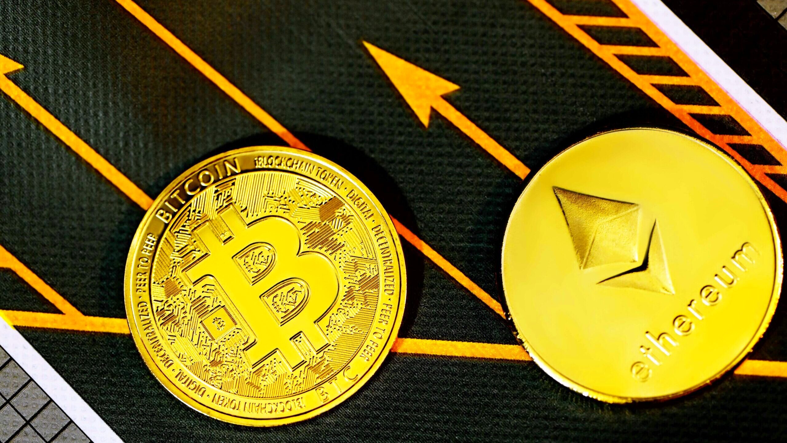Two gold coins bearing the bitcoin and ethereum logos are laid on a flat surface.
