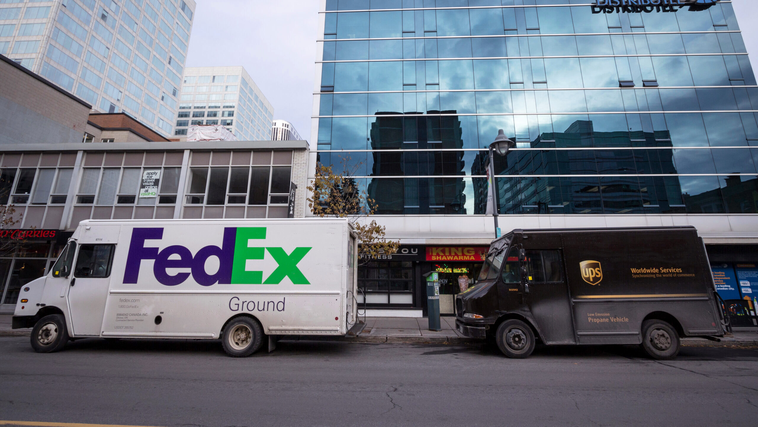 A FedEx delivery truck and UPS delivery truck are shown parked next to each other outside a building.