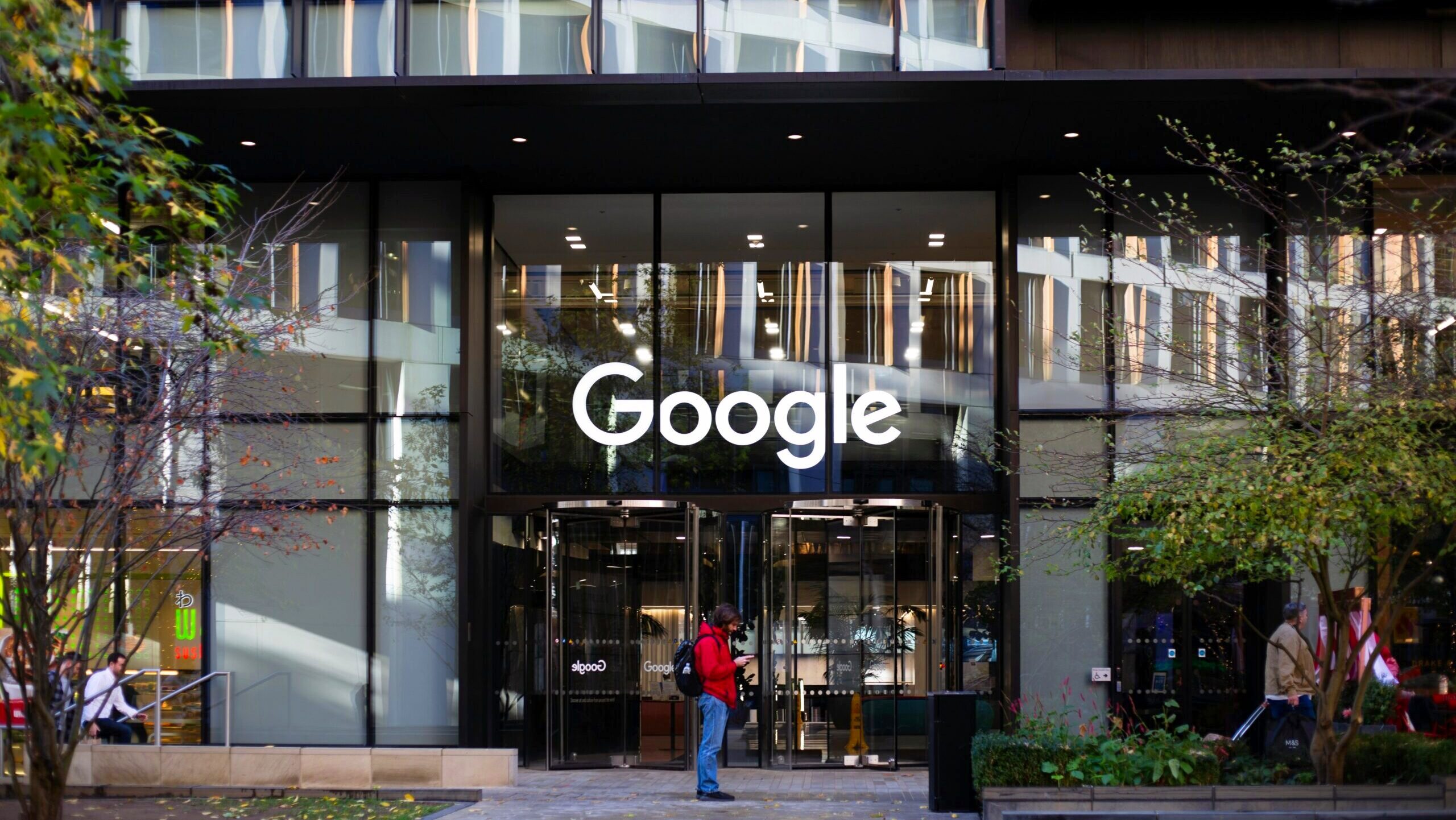 A person is shown standing outside a Google office, where the company's text logo is emblazoned on the front windows.