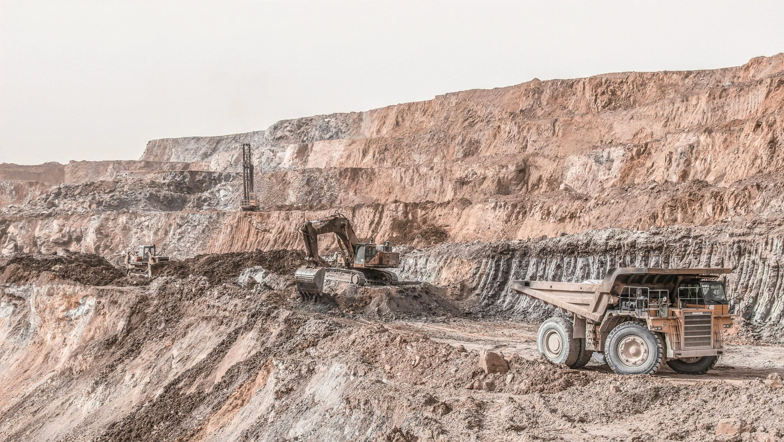 Multiple large mining vehicles are shown working a copper mine along a series of rocky cliffs.