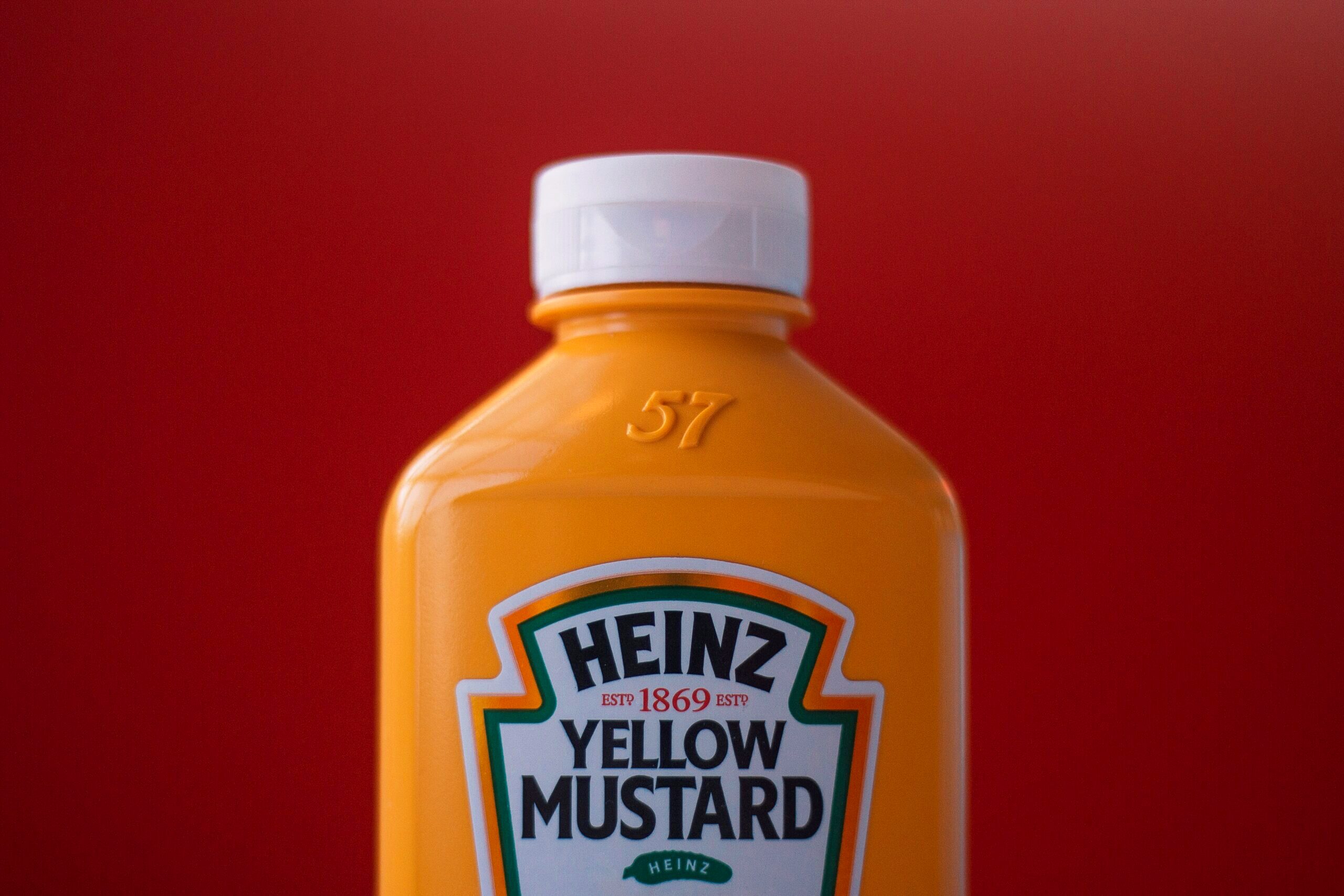 A bright yellow plastic container of Heinz mustard is shown in front of a bright red background.