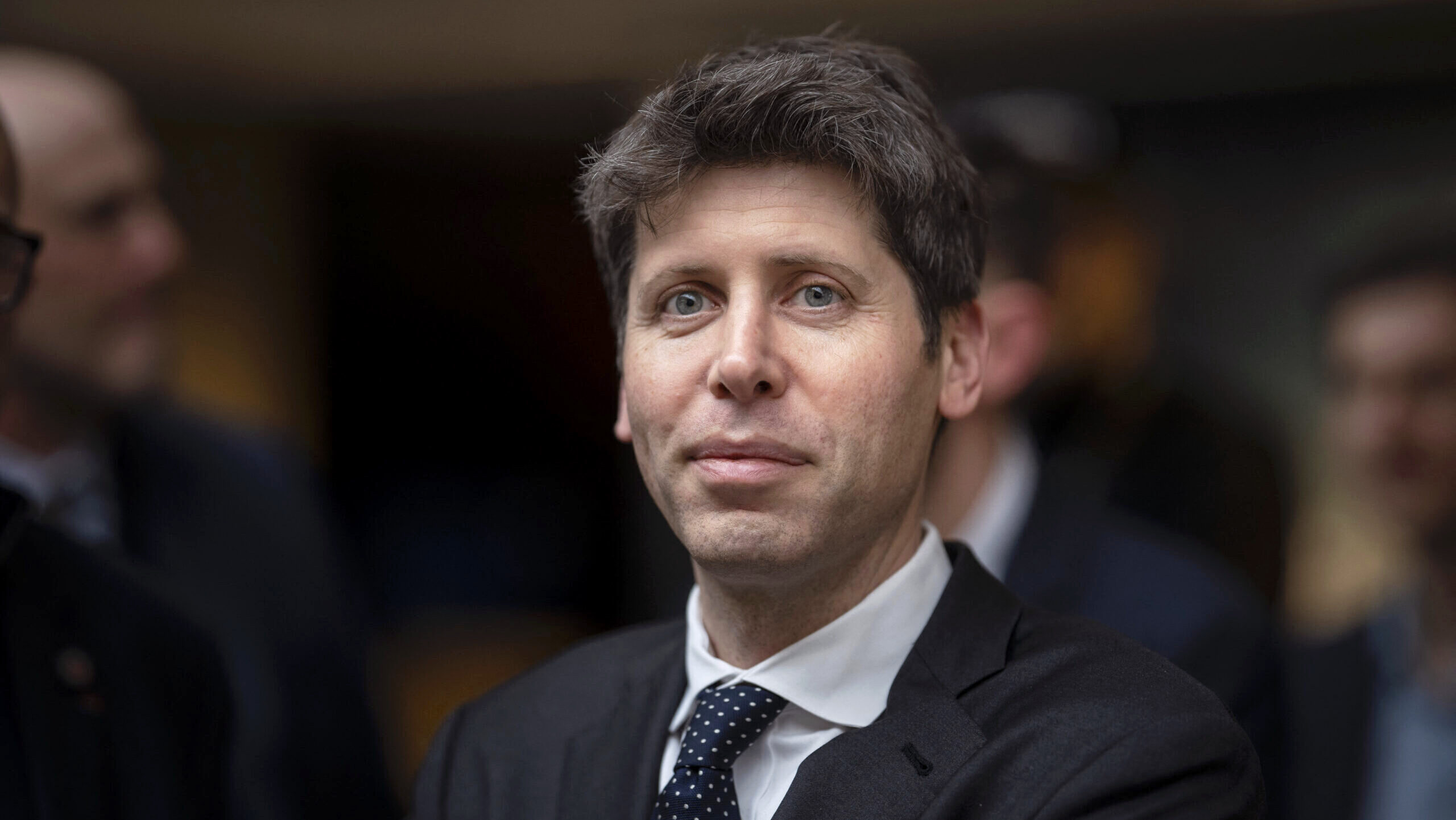 Sam Altman, CEO of OpenAI, is shown smiling at the Artificial Intelligence Action Summit in Paris.