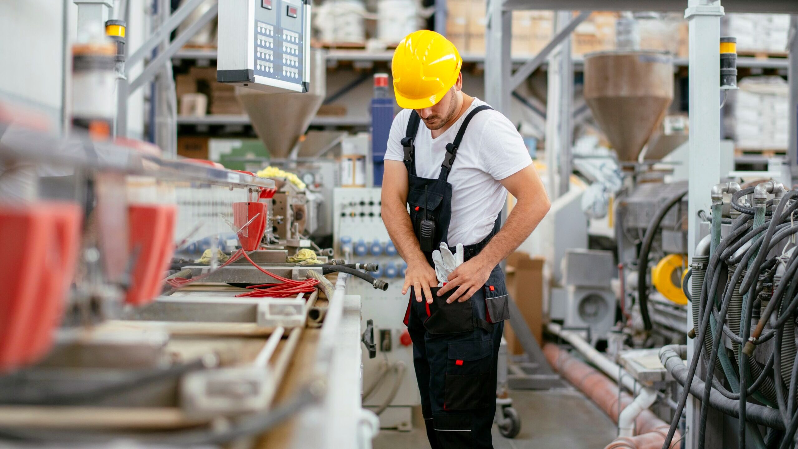 A factory worker adjusts his gloves in a utility pouch at his waist.