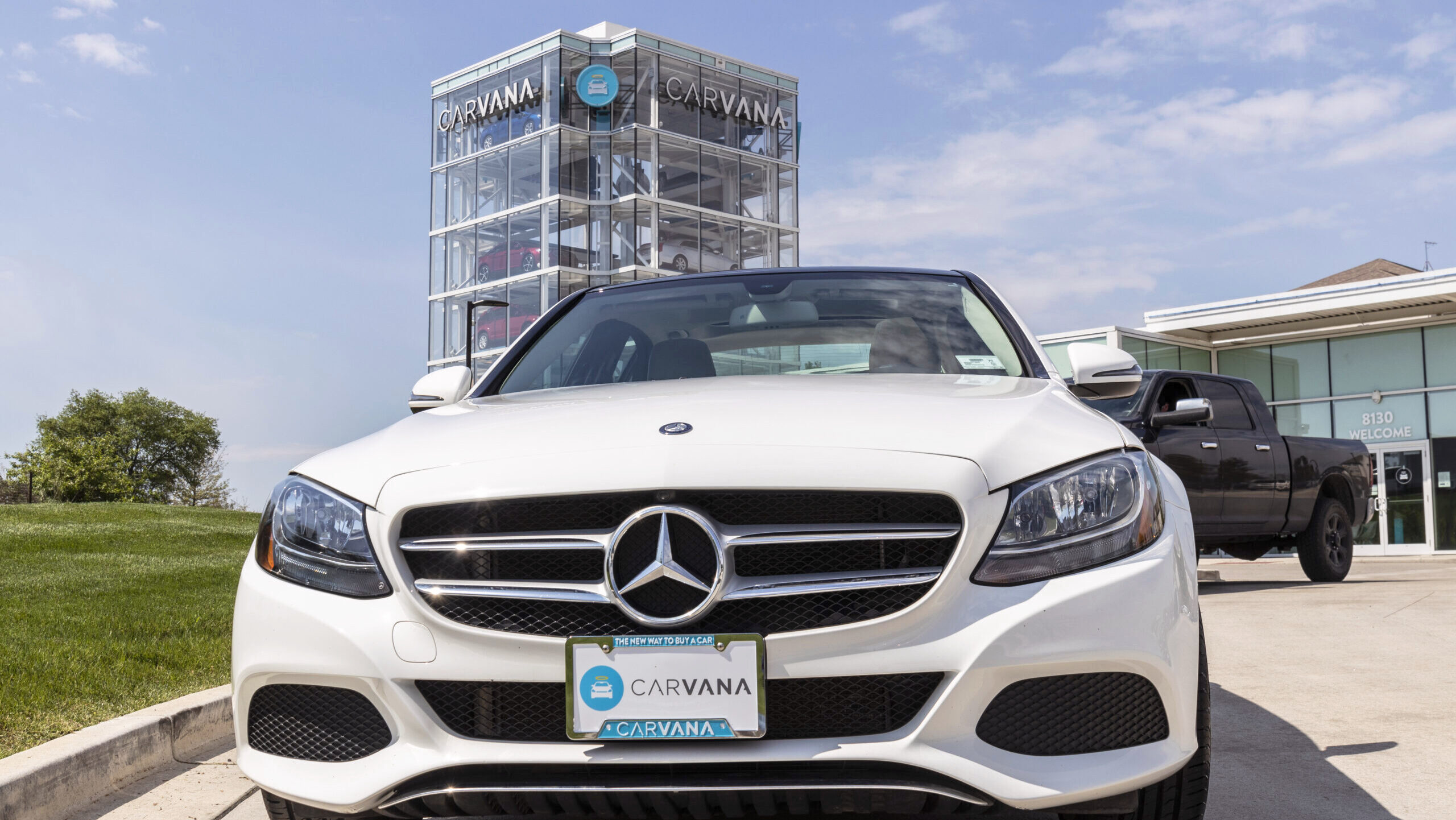 A Carvana used car vending machine is shown in the background of a parked Mercedes-Benz car with a Carvana license plate.