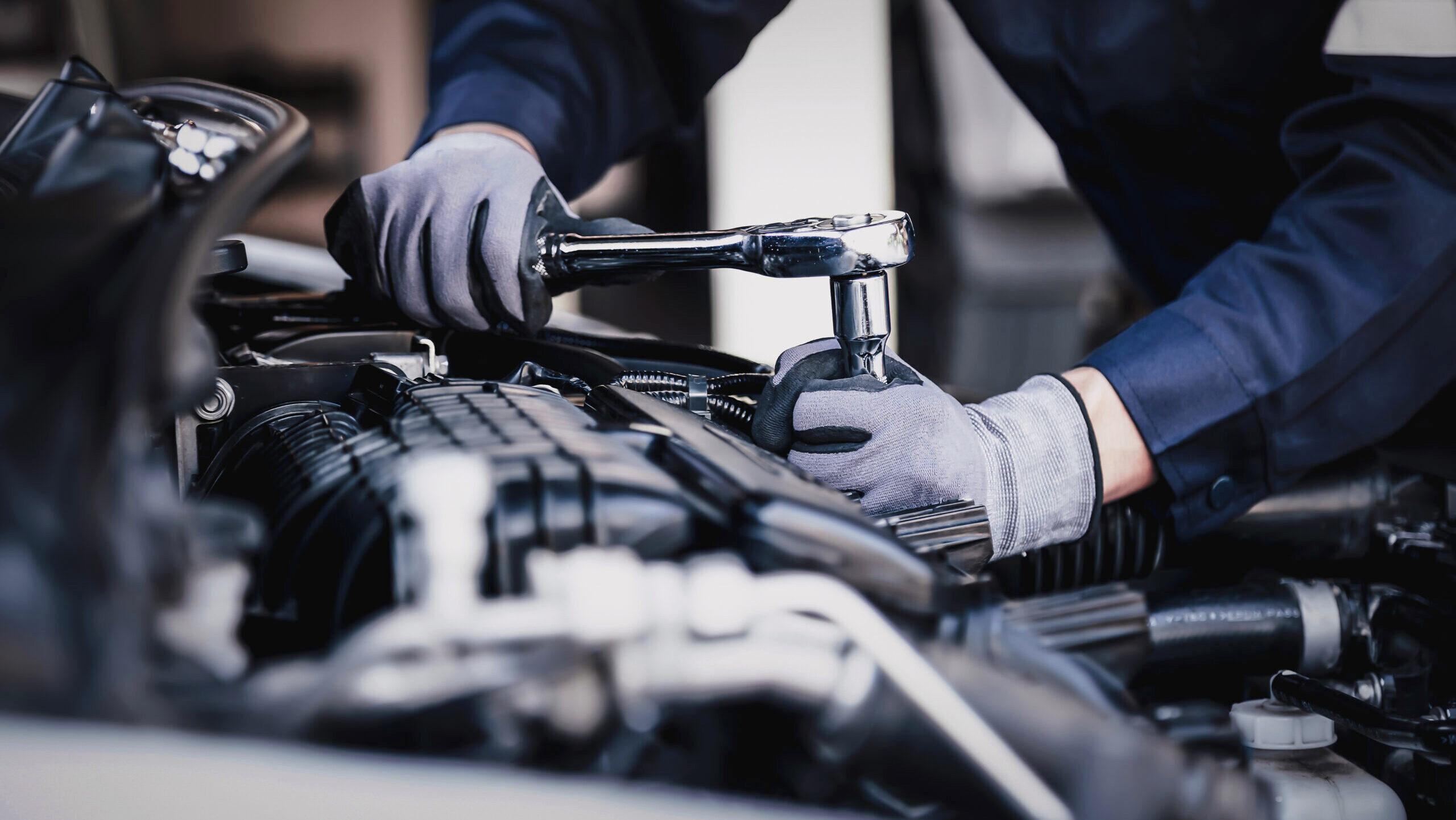A car mechanic is shown working on the engine of a vehicle in a garage.