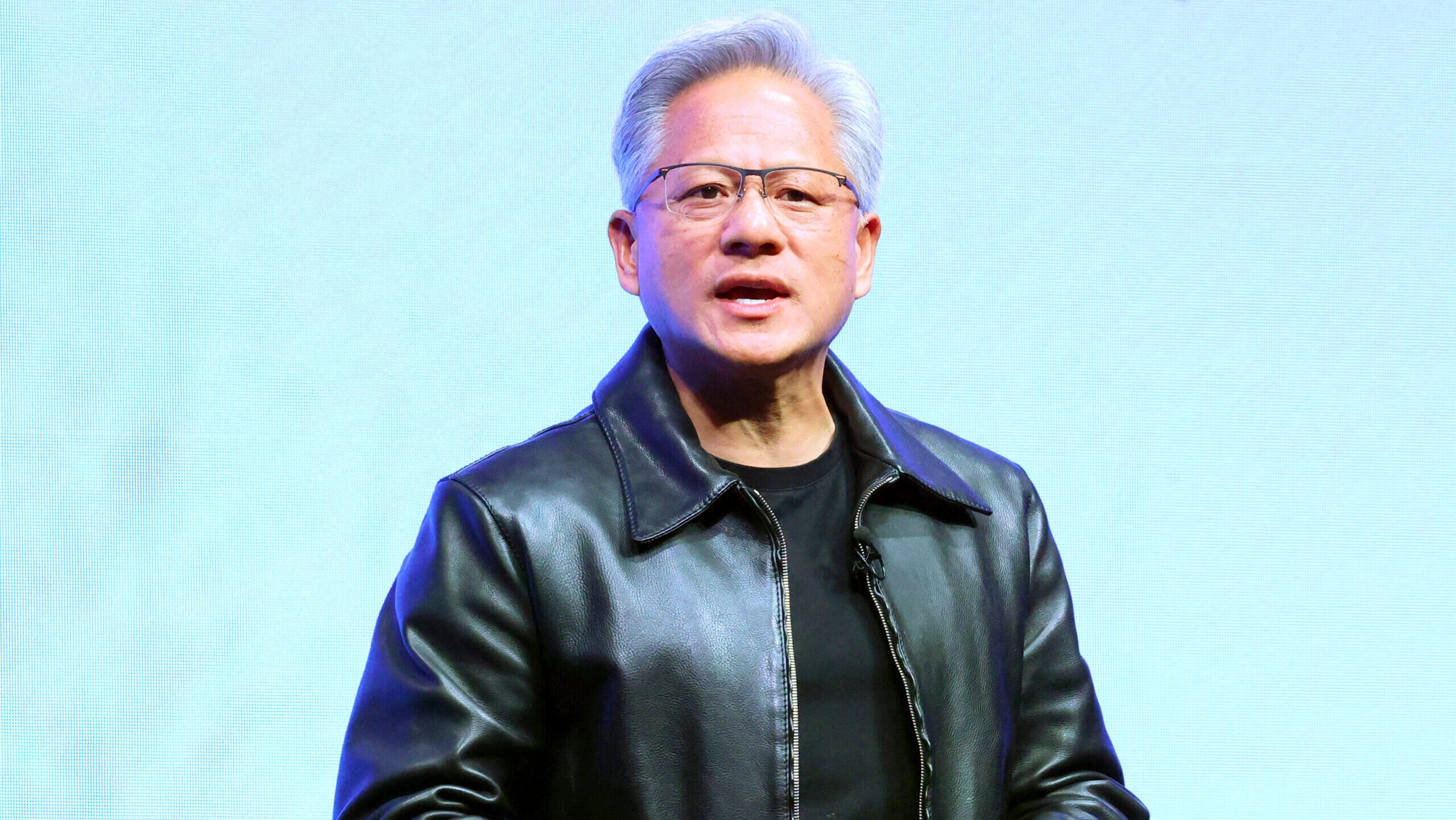 Nvidia CEO Jensen Huang, wearing his trademark black leather jacket, is seen addressing a crowd on stage.