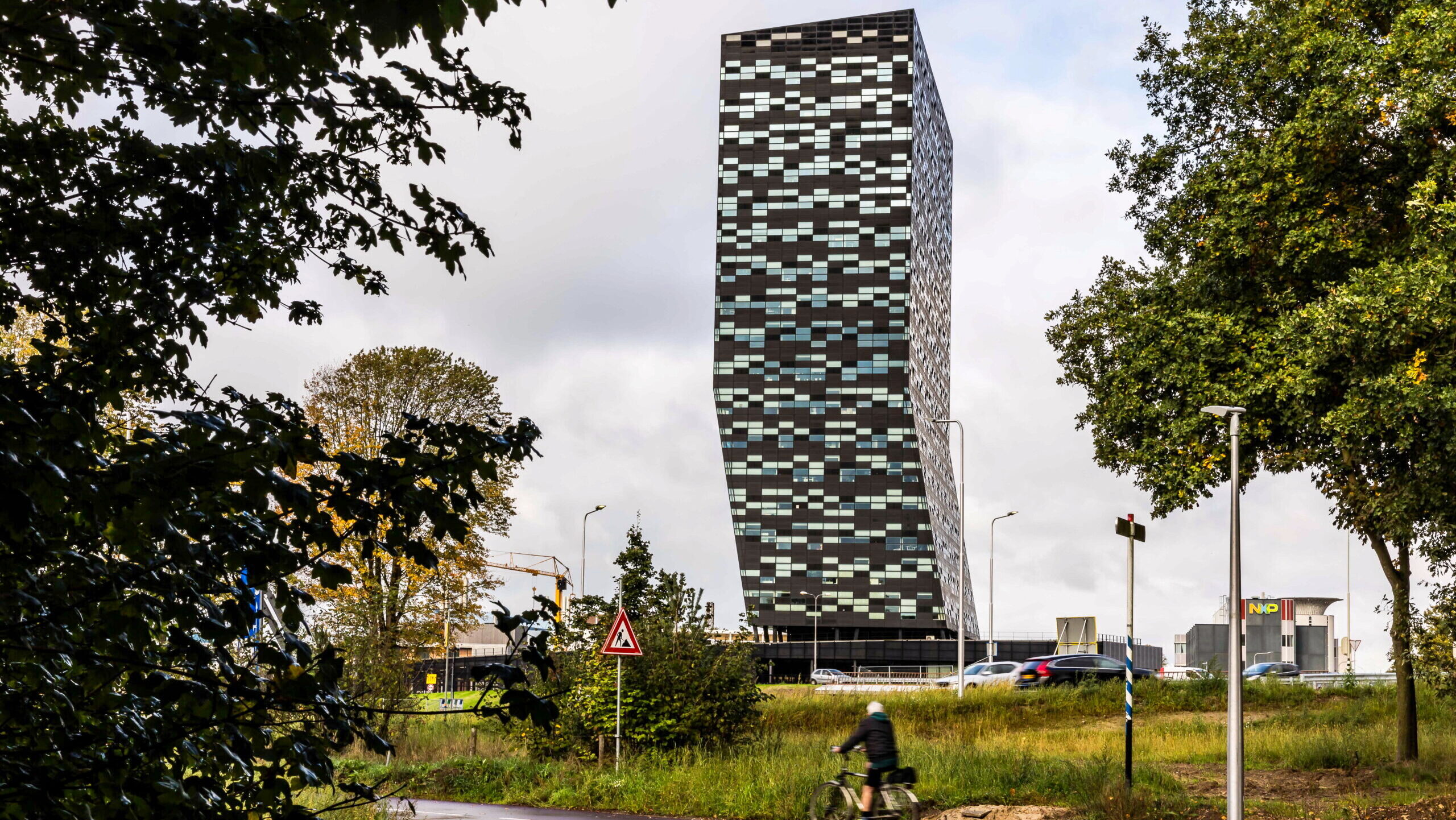 The tall, freestanding headquarters of Nexperia in the Dutch city of Nijmegen is shown as cars and a cyclist ride by in the foreground.