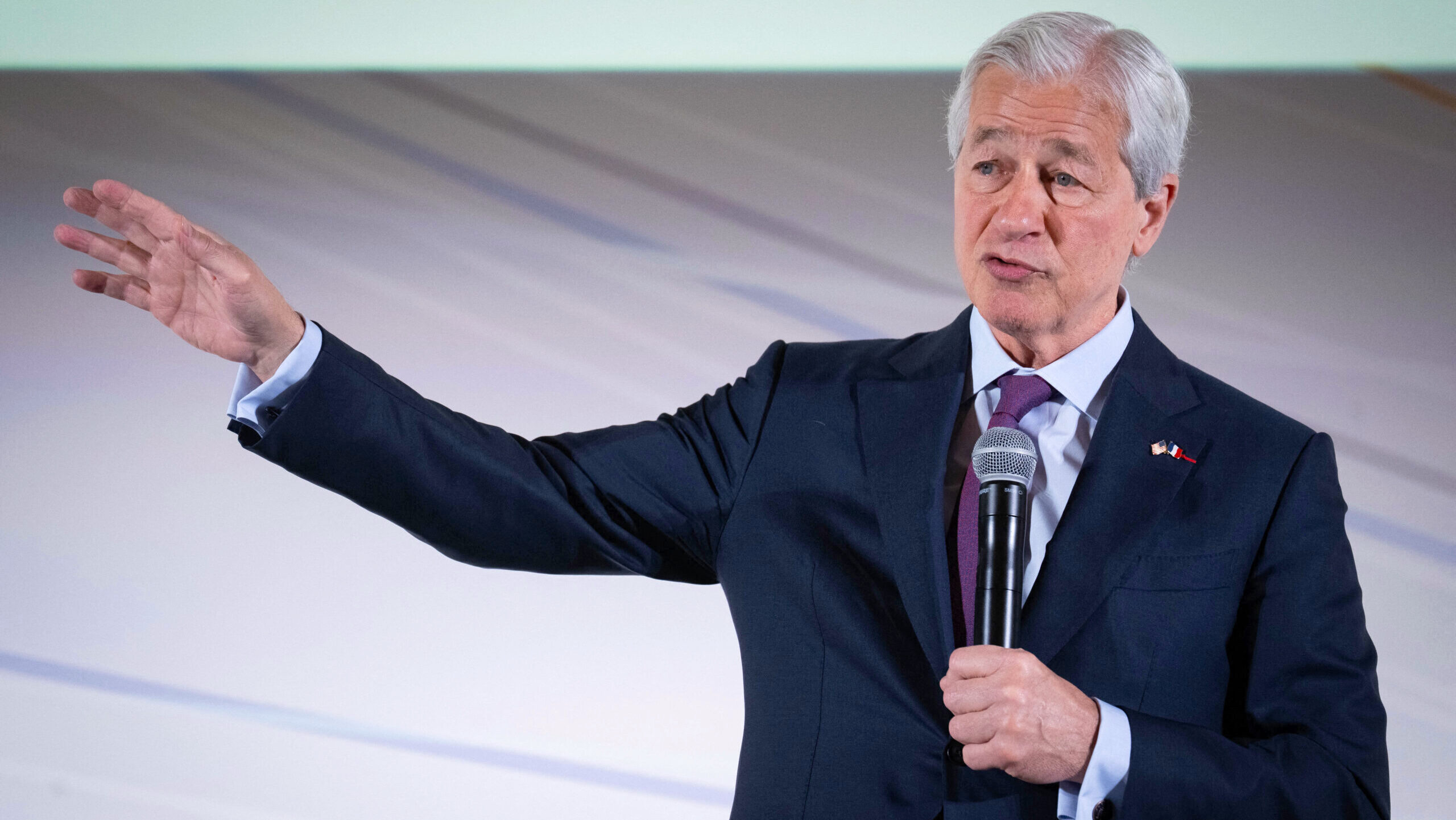 JP Morgan CEO Jamie Dimon gestures with his right arm outstretched while speaking to a crowd on stage.