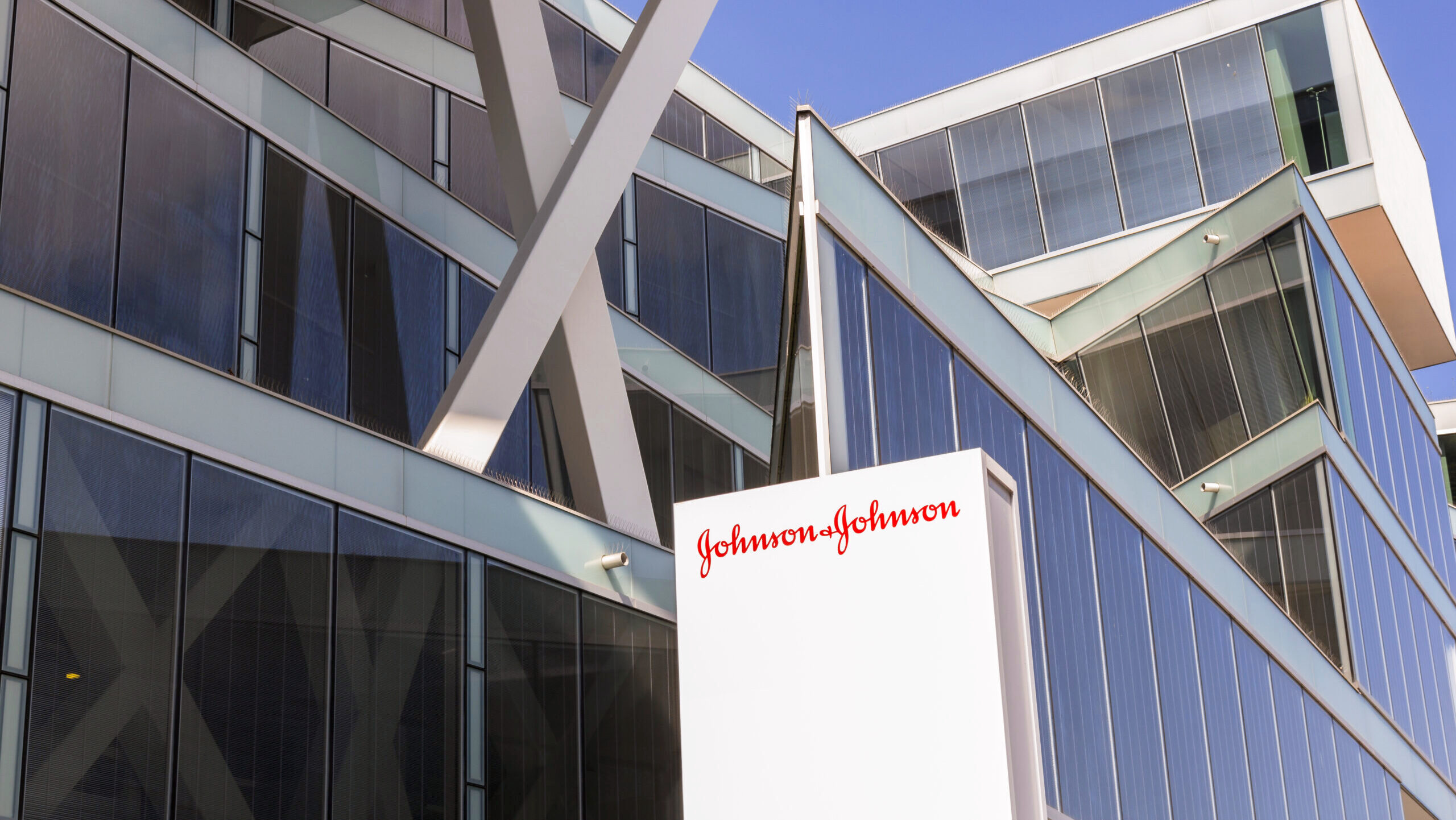 The front of a Johnson and Johnson office with modern, angular architecture is shown against a blue sky.