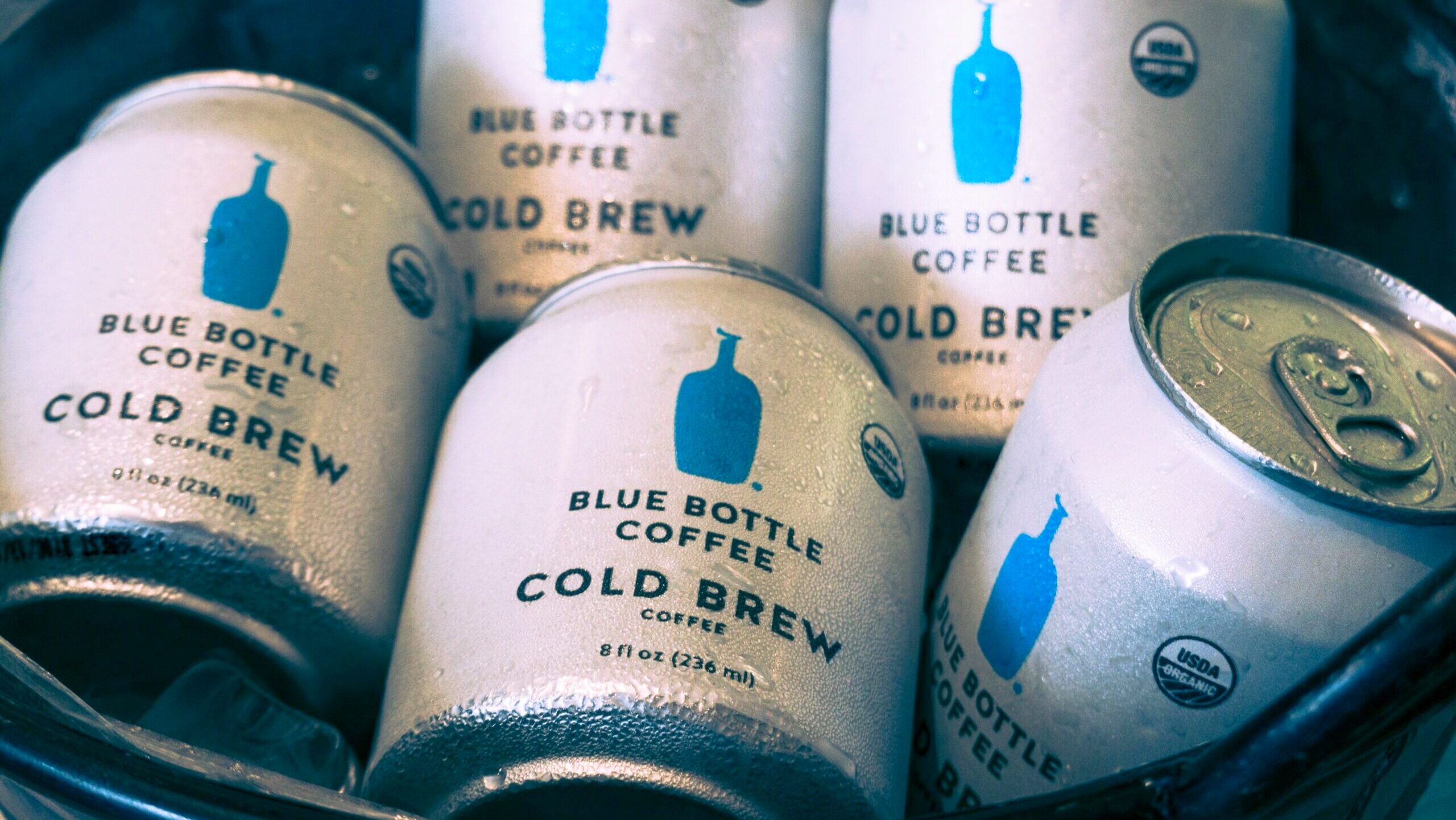Chilled cans of Blue Bottle Coffee cold brew are displayed in an ice bucket.