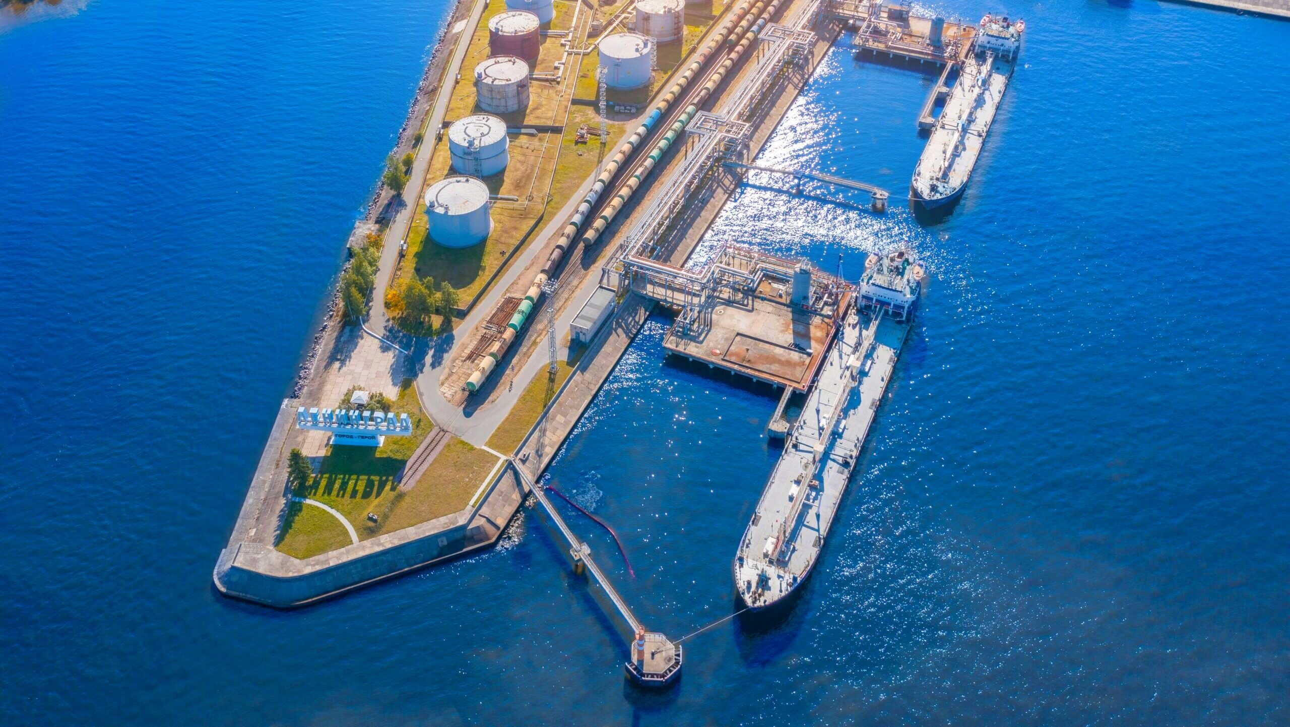 Ships are shown docked at a harbor with an oil refinery and rail depot.