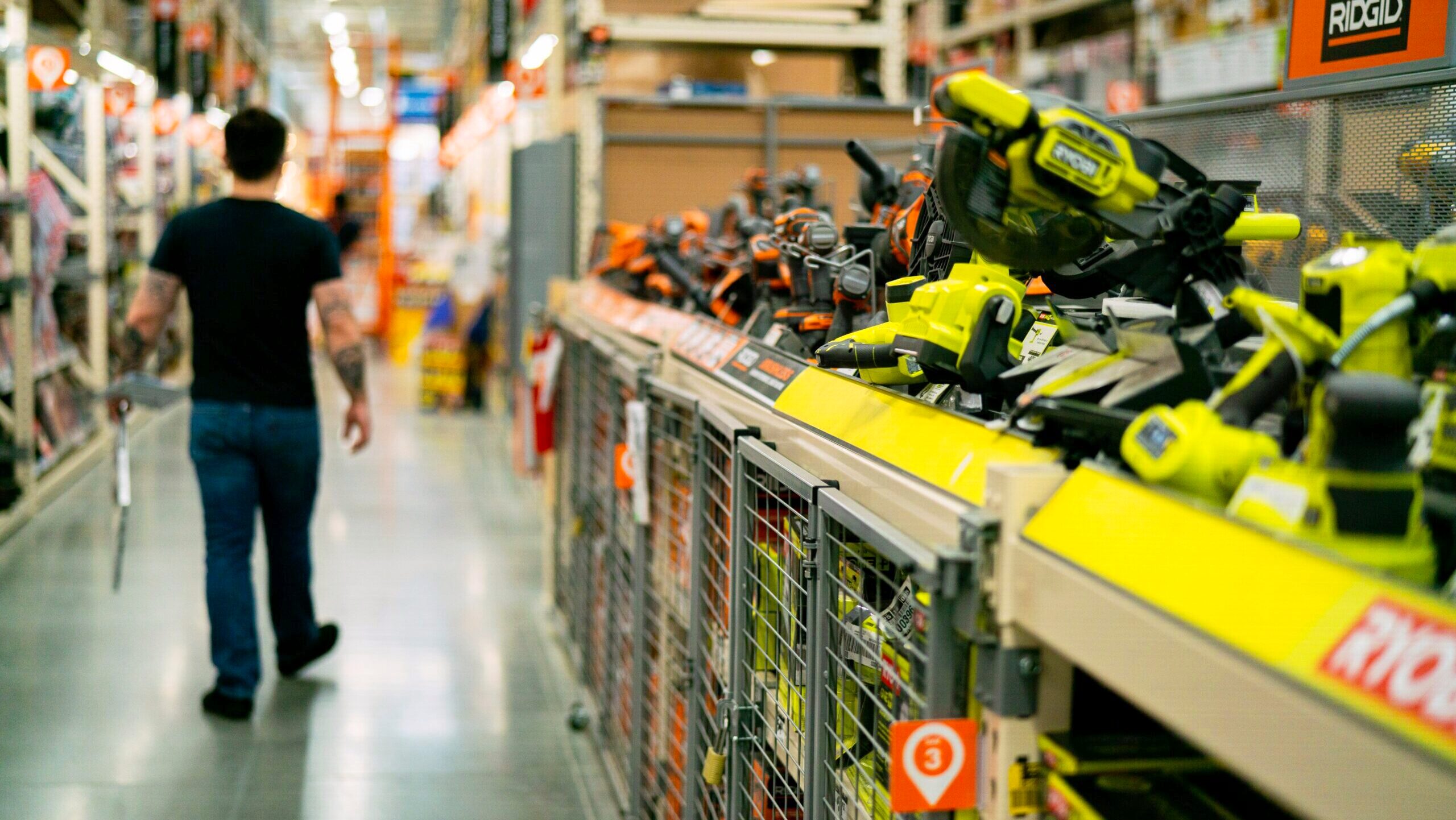 Power tools are on display in a Home Depot aisle as a customer walks away from the direction of the camera.