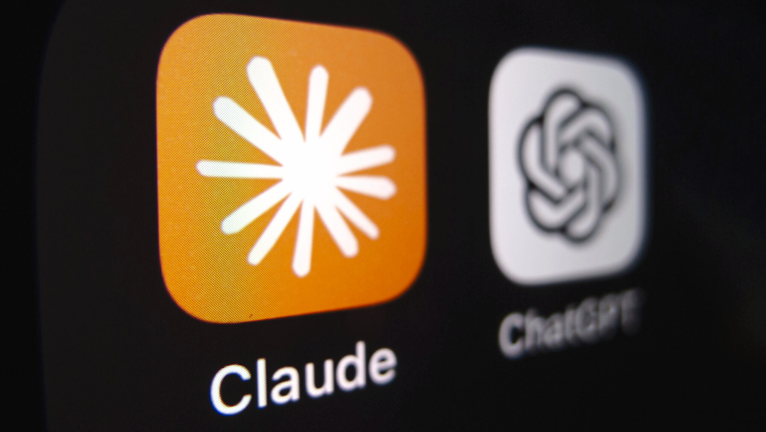 The Claude icon is shown in the foreground on a screen, with the ChatGPT icon blurred in the background.