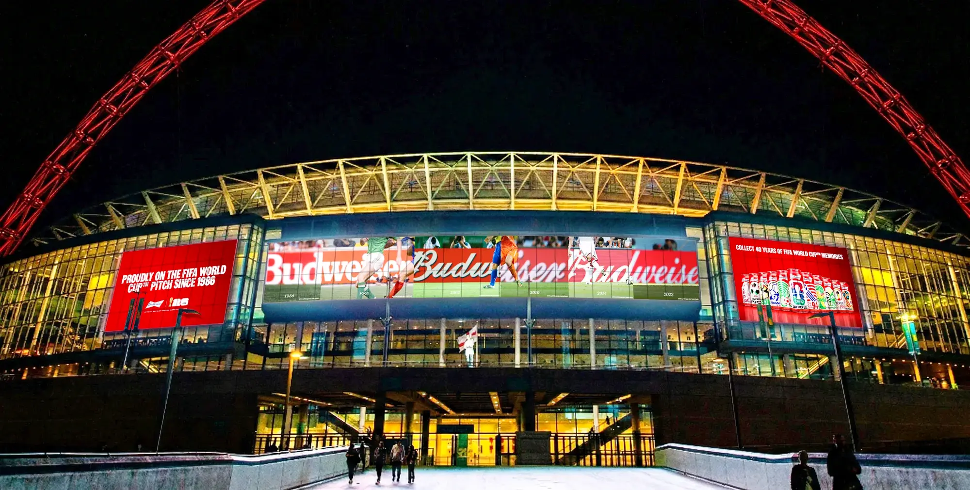 Budweiser soccer adverts are shown on the front of a stadium at night.