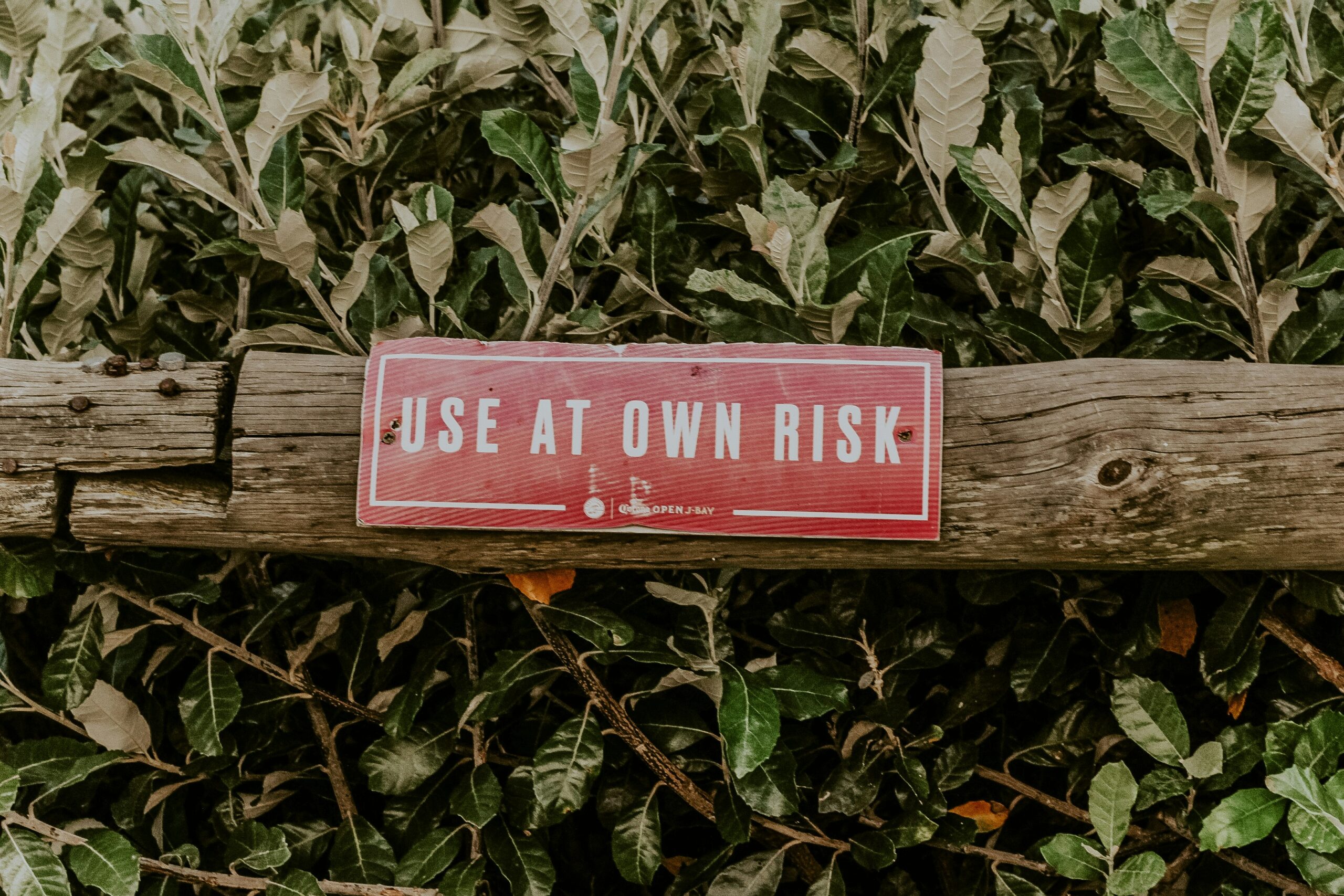 Photo of a red sign over a leafy background that reads 'use at own risk.'