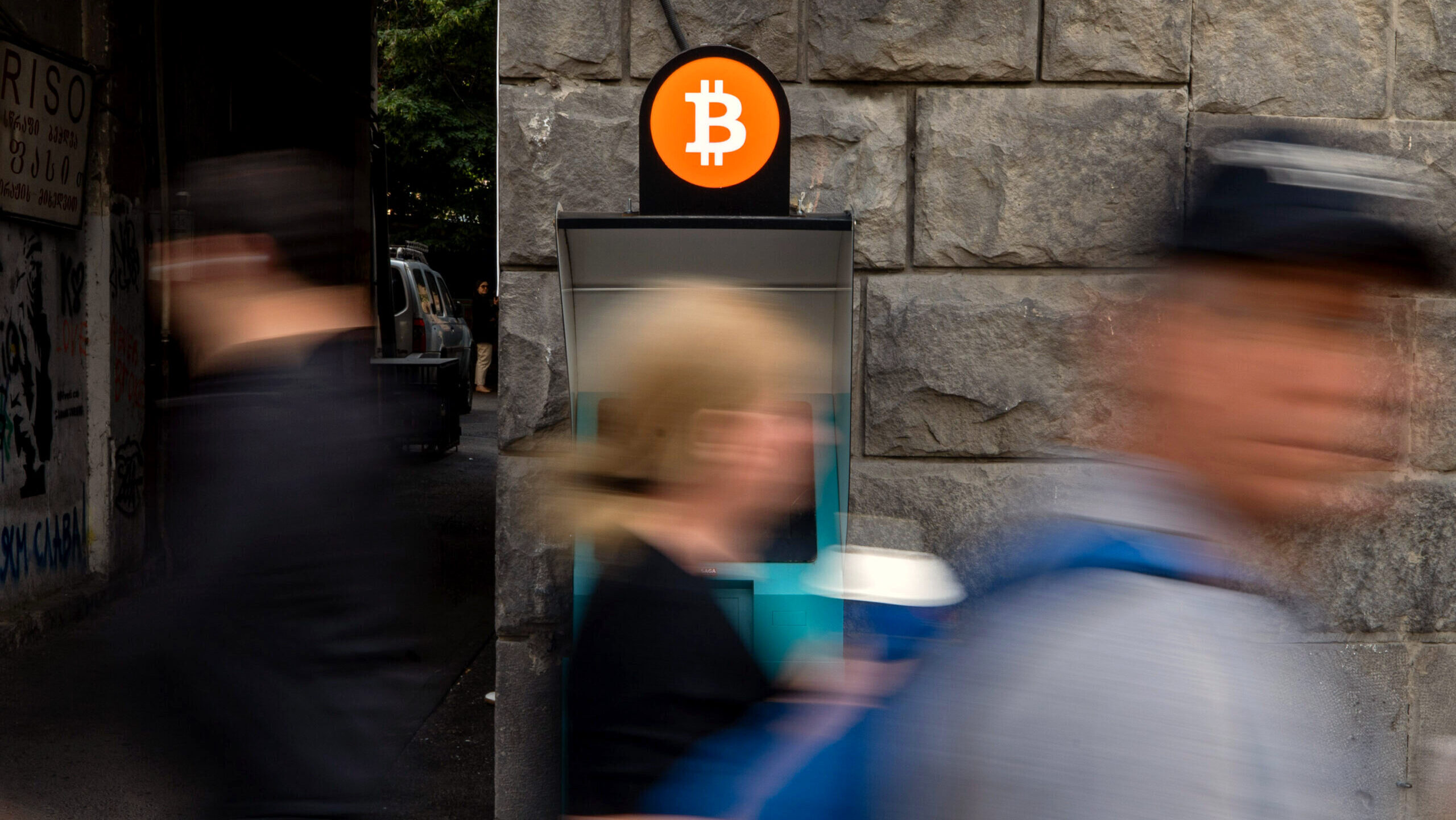 Photo of a people walking past a Bitcoin ATM.