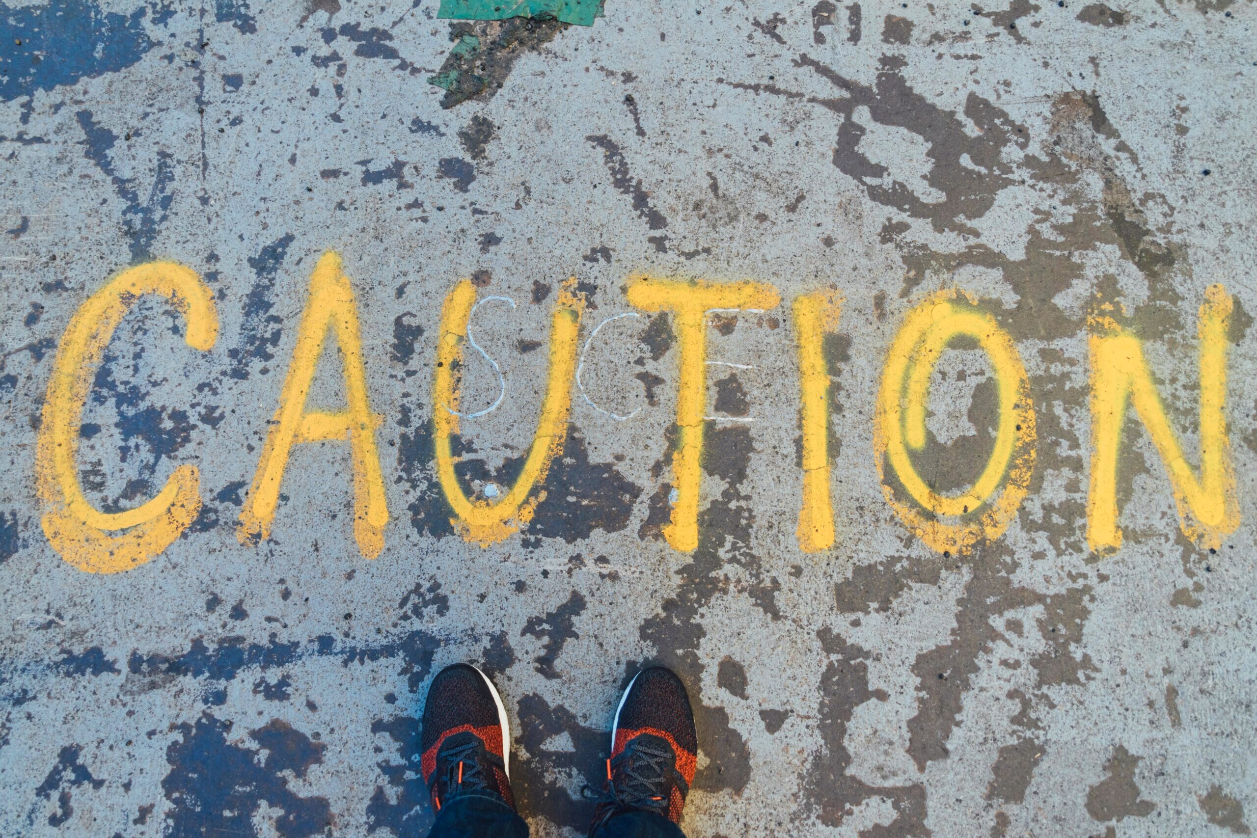 Photo of the word "caution" spray painted in yellow on the ground.