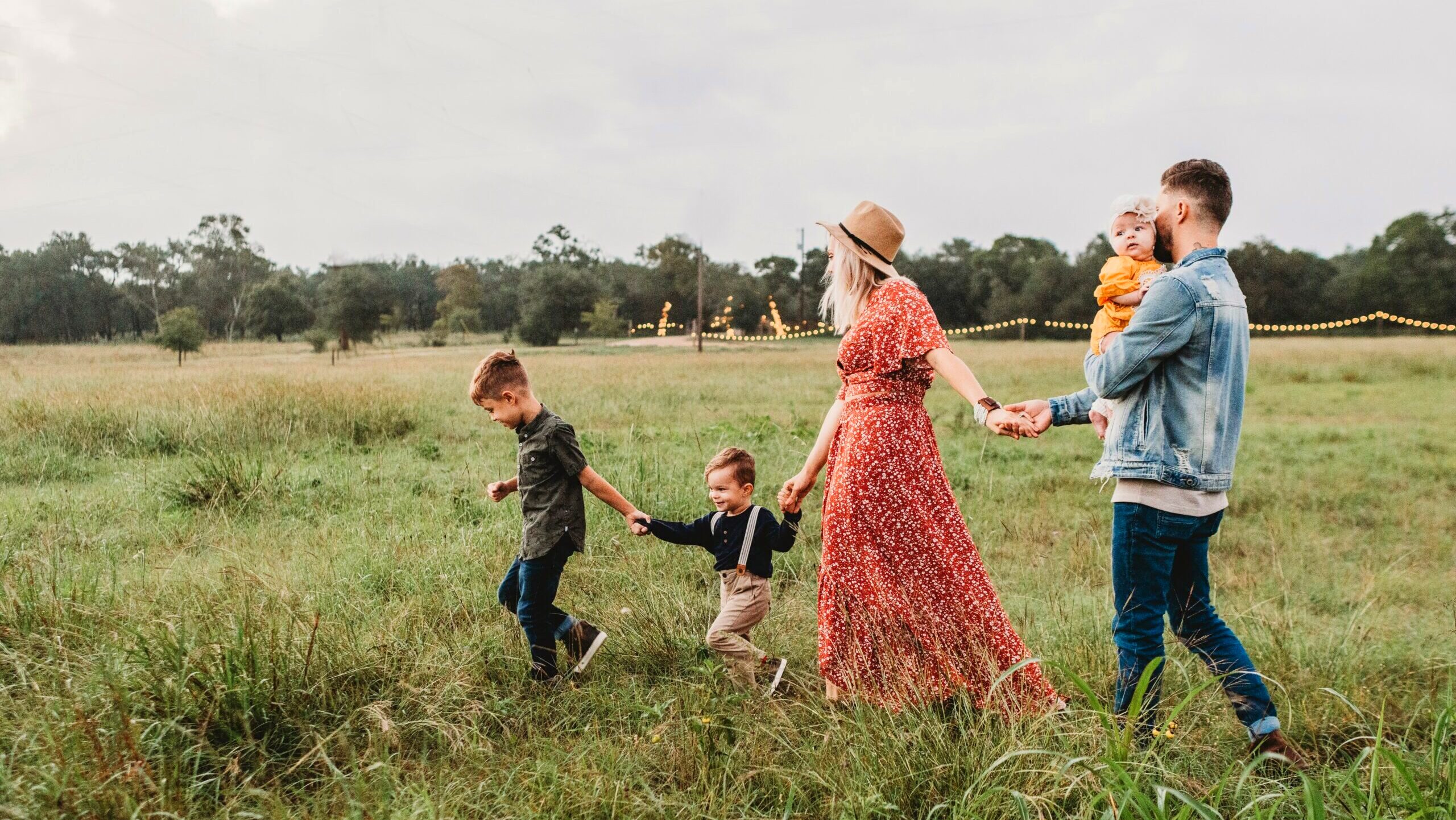A family consisting of two parents and three kids walks together, holding hands, across a field.